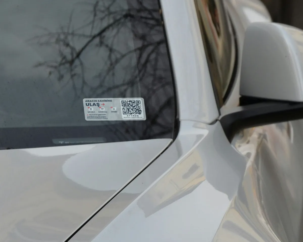 Beyaz bir Tesla'nın ön camının köşesine yapıştırılmış Sahibine Yaz sticker'ı